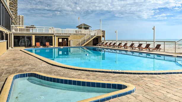 Une piscine dont le bord est revêtu de carrelage, une tour de surveillance pour les sauveteurs et des chaises longues disposées le long du bord de la piscine.