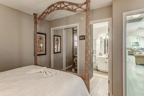 A bedroom with a four-poster bed, a large mirror, and a view into the bathroom.