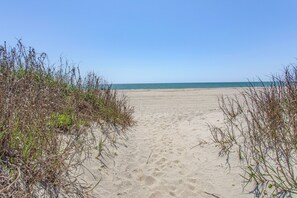 A sandy beach path leading to the ocean, surrounded by vegetation.