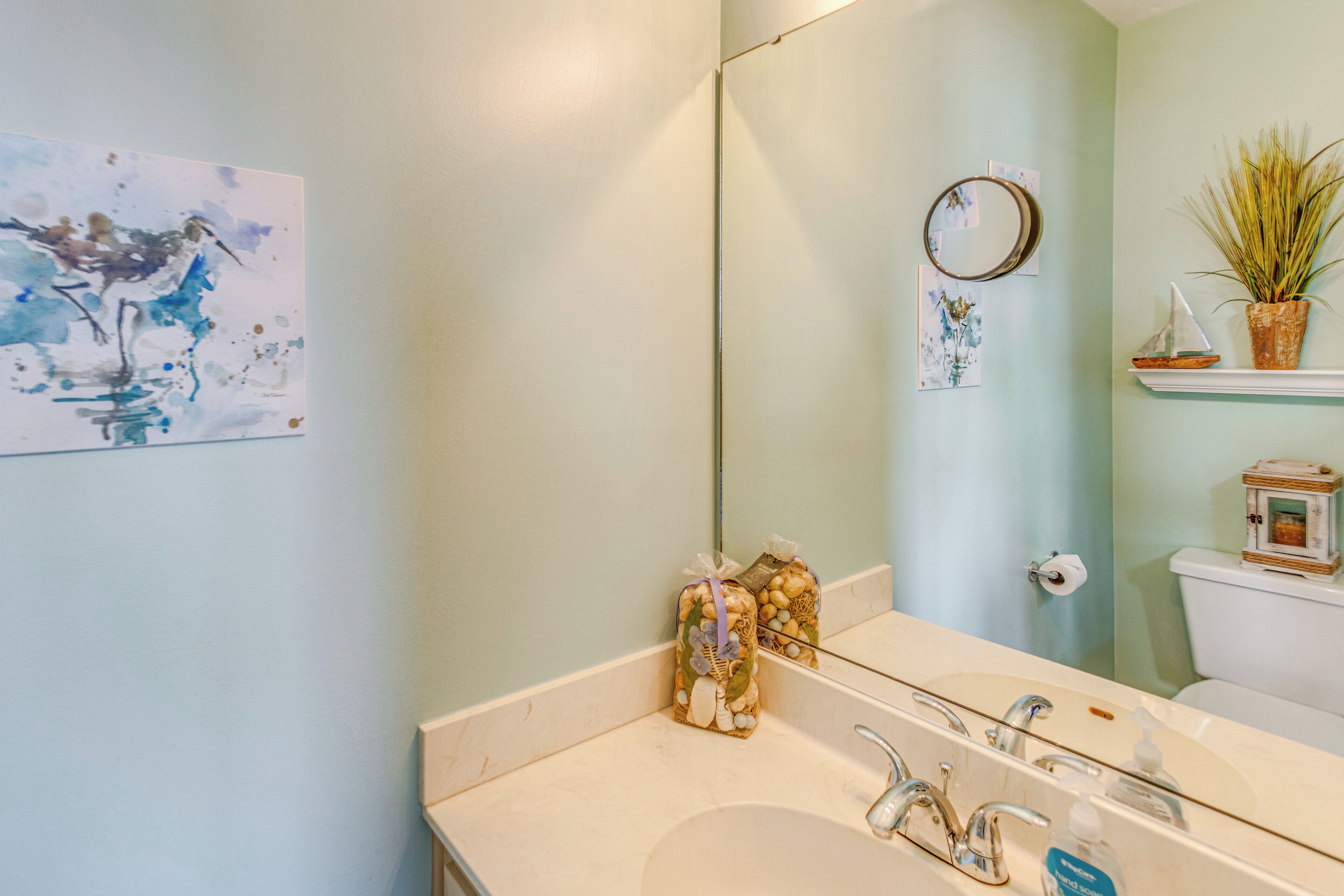 Un baño con lavamanos blanco, espejo y estante en la pared con objetos decorativos.
