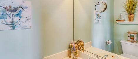 Un baño con lavamanos blanco, espejo y estante en la pared con objetos decorativos.