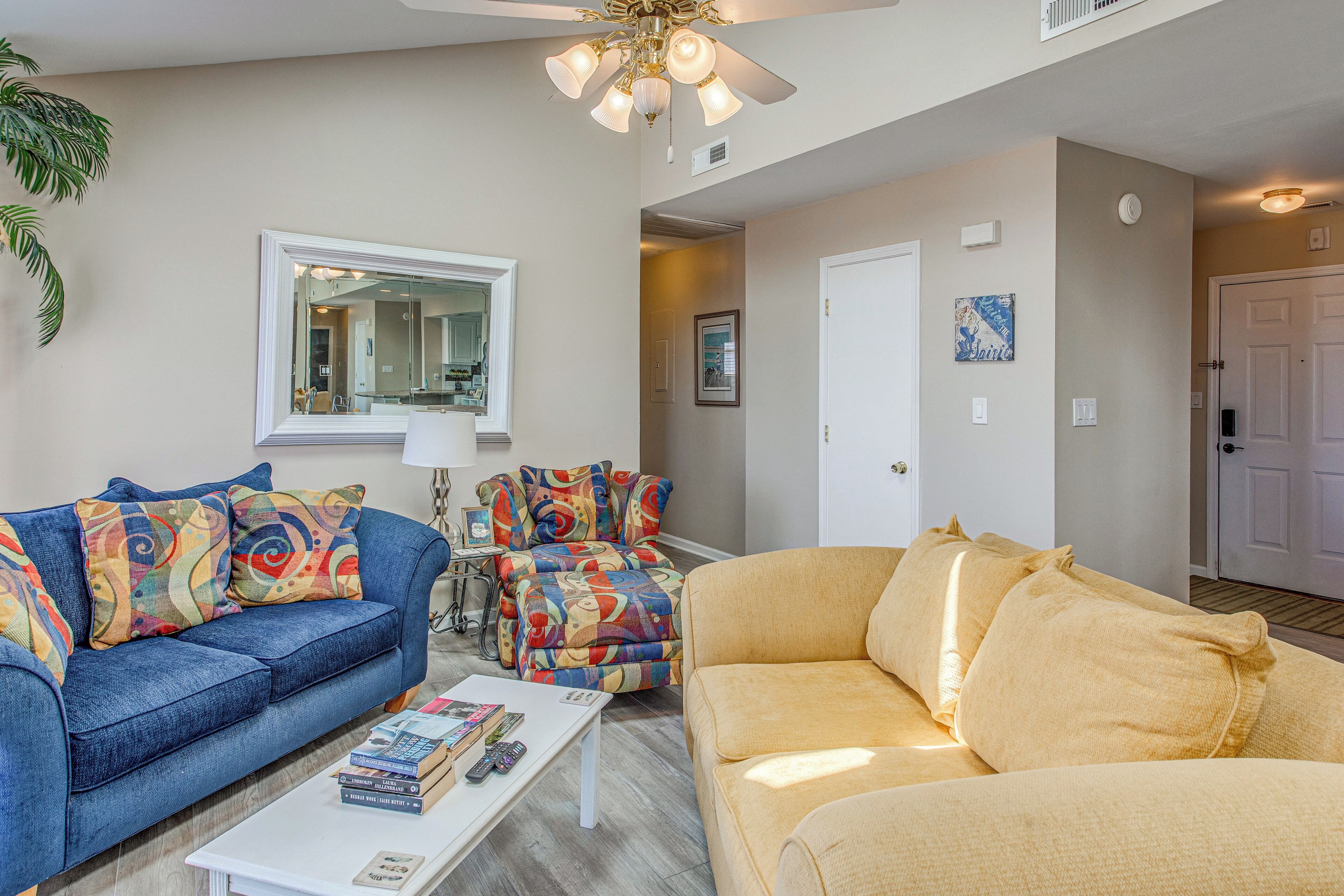 A living room with a blue sofa, a yellow sofa, a coffee table, and a ceiling fan.