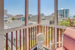 A balcony with a wicker chair and a cushioned seat, overlooking a residential area with various houses and a tall building in the distance. - Walk to Beach! North Myrtle Beach Condo w/ Balcony (North Myrtle Beach)