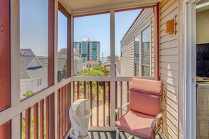 A balcony with a wicker chair and a cushioned chair, a fan, and a view of neighboring buildings. - Walk to Beach! North Myrtle Beach Condo w/ Balcony (North Myrtle Beach)