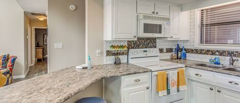 A kitchen with white cabinets, a microwave, a sink, and a granite countertop.