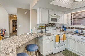 A kitchen with white cabinets, a microwave, a sink, and a granite countertop.