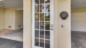 A white door with a window, a garage door, and a wall-mounted light fixture. - Walk to Bahia Beach! Canal-front Townhome w/ Views (Ruskin)