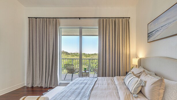 A bedroom with a large bed, a view of the outdoors, and a balcony with chairs. - Walk to Bahia Beach! Canal-front Townhome w/ Views (Ruskin)