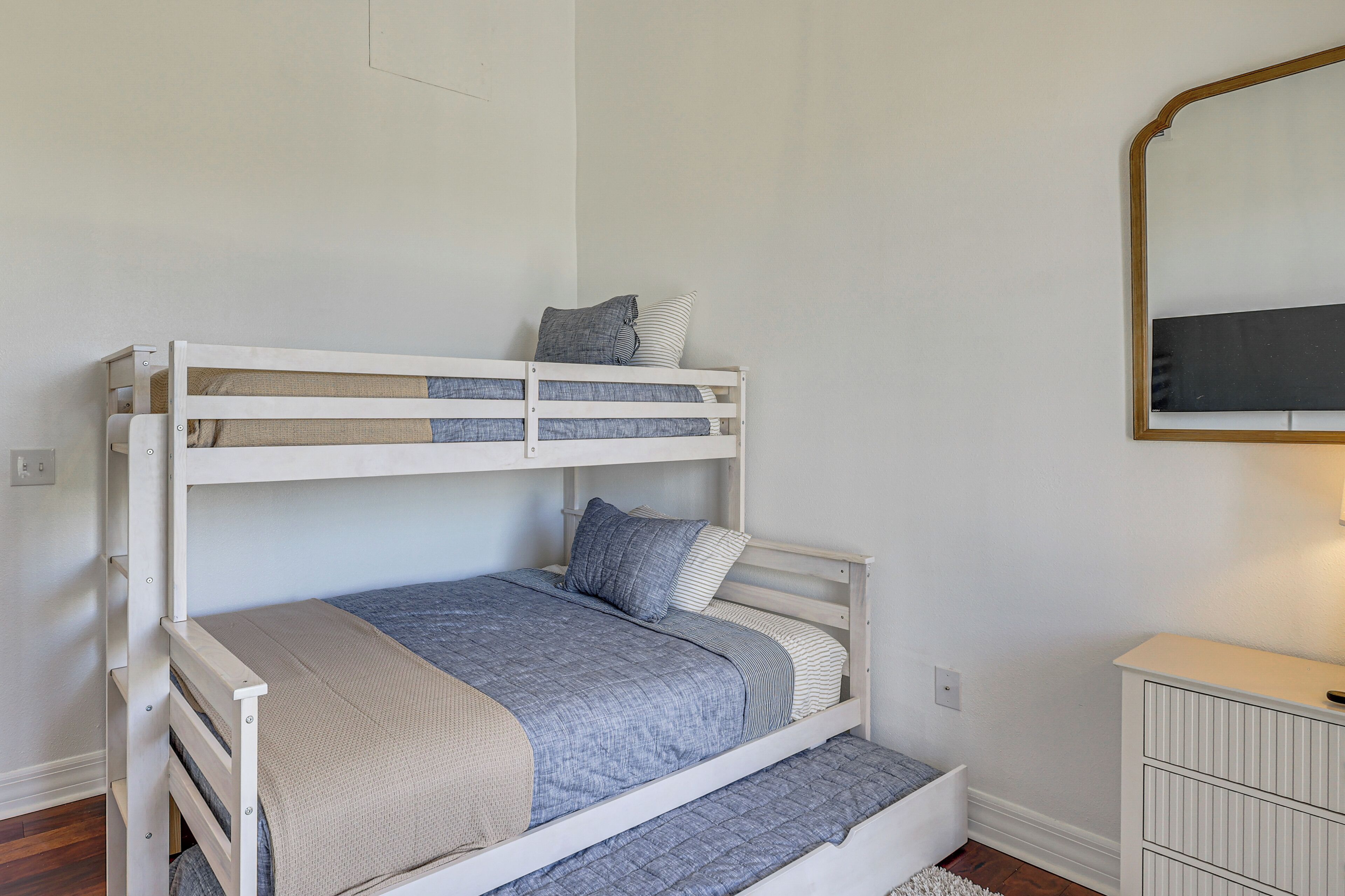 A bunk bed with a lower bed and a bunk above, a dresser, and a mirror on the wall.