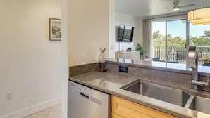 A kitchen with a double sink, a dishwasher, a flat-screen TV, and a ceiling fan. - Walk to Bahia Beach! Canal-front Townhome w/ Views (Ruskin)