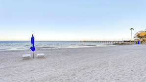 A beach with two white lounge chairs, a blue umbrella, and a pier in the background. - Walk to Bahia Beach! Canal-front Townhome w/ Views (Ruskin)