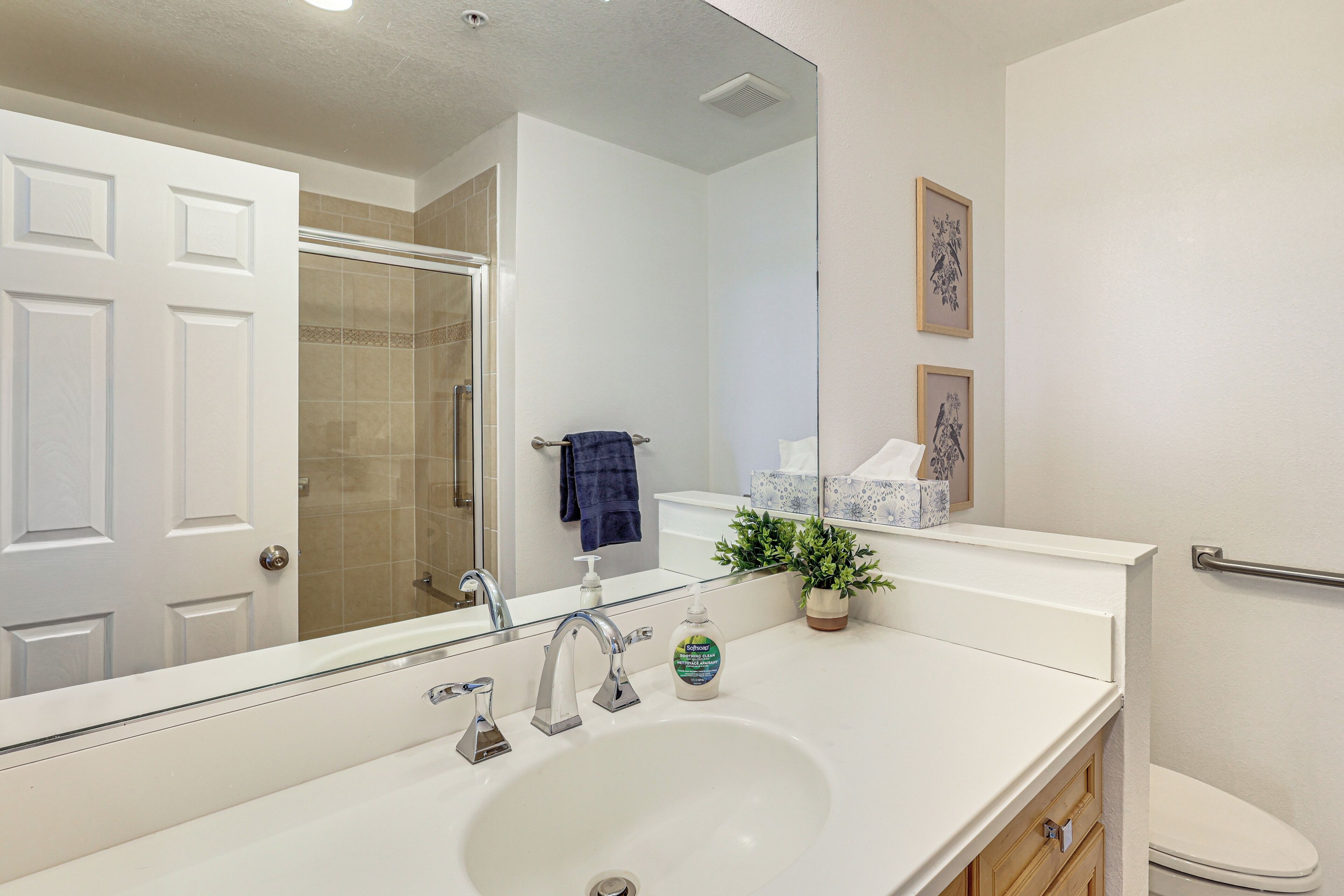 A bathroom with a white sink, a mirror, a shower, a toilet, and a towel rack.