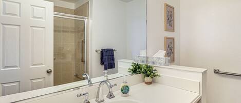 A bathroom with a white sink, a mirror, a shower, a toilet, and a towel rack.
