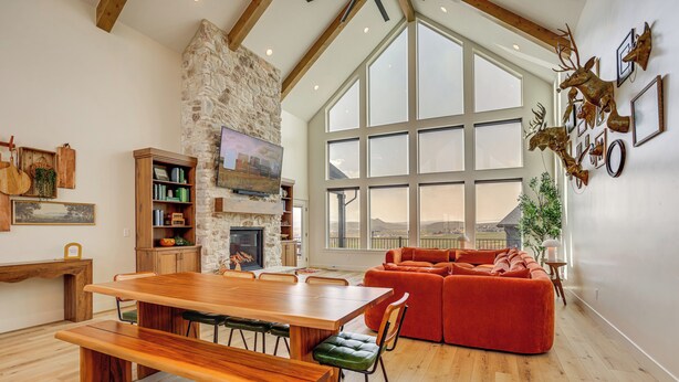 A spacious living area with a large wooden dining table, a red sofa, and a stone fireplace. - Luxury Bear Lake Getaway w/ Sports Court & Hot Tub (Garden City)