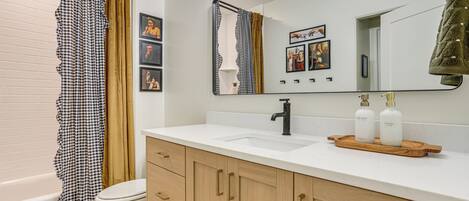 A bathroom with a white sink, a mirror, and a toilet. There are two bottles of hand soap on the sink.