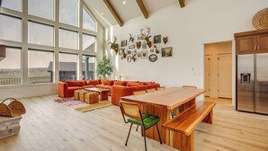 A spacious living area with a large window, a wooden dining table, and a modern kitchen. - Luxury Bear Lake Getaway w/ Sports Court & Hot Tub (Garden City)