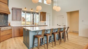 A modern kitchen with a large island, bar stools, and wooden cabinetry. - Luxury Bear Lake Getaway w/ Sports Court & Hot Tub (Garden City)