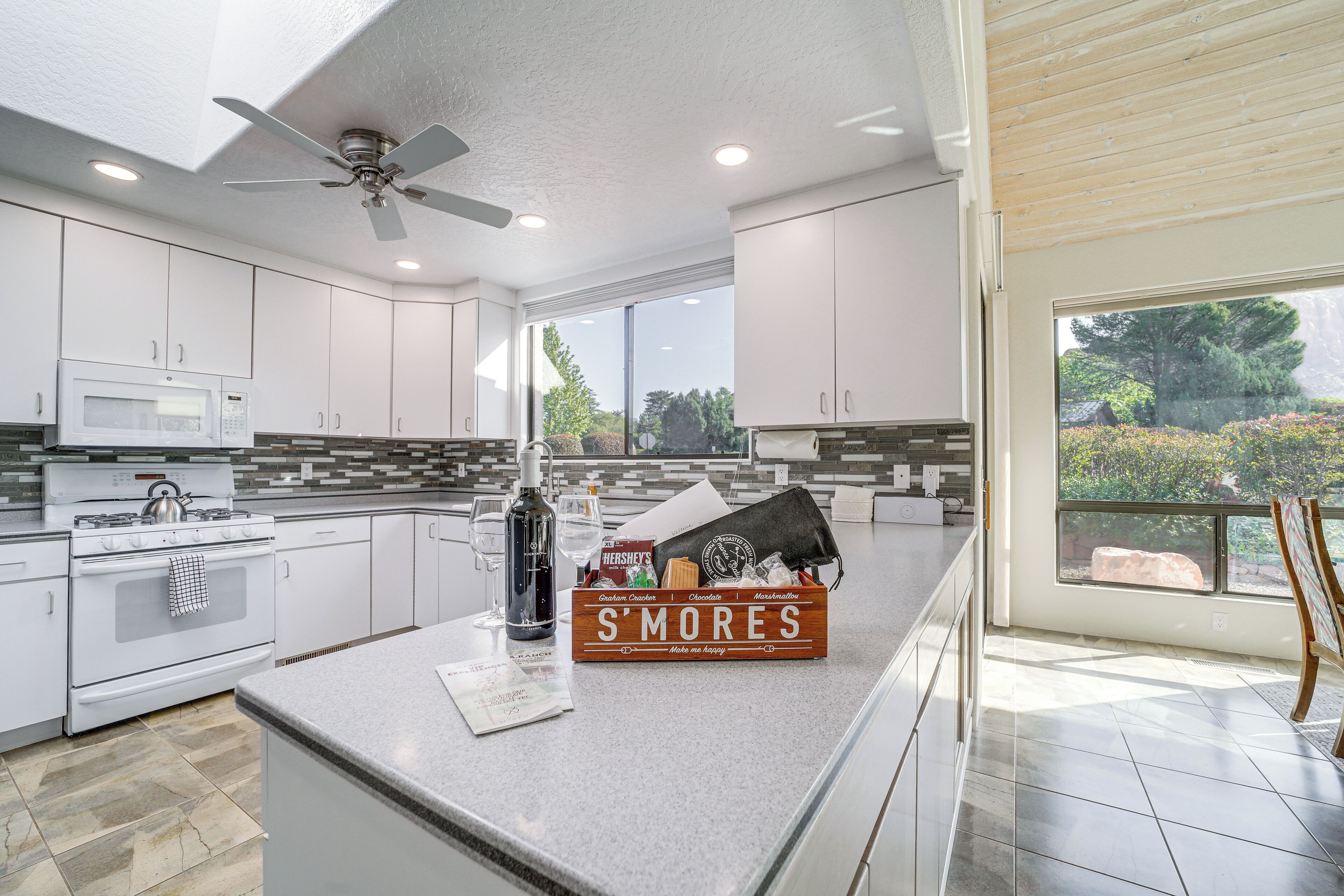 A modern kitchen with white cabinets, a stainless steel stove, a microwave, and a large window offering a view of greenery.