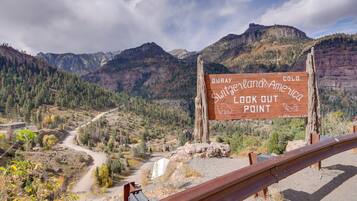 A wooden sign with text, a road, and mountainous terrain.