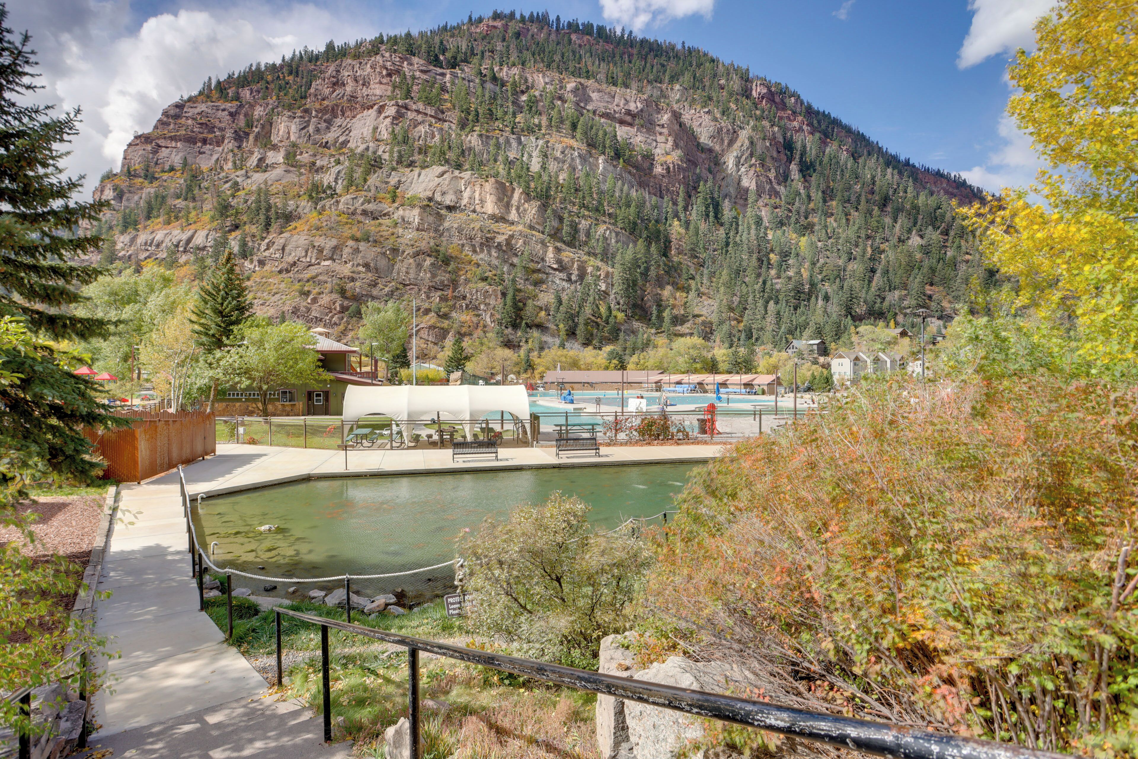 A mountain landscape with a swimming pool, a pathway, and a building with a white roof.