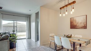 A modern dining area with a wooden table, white chairs, and a hanging light fixture. - Fenced Yard + Outdoor Games: Buckeye Home! (Buckeye)