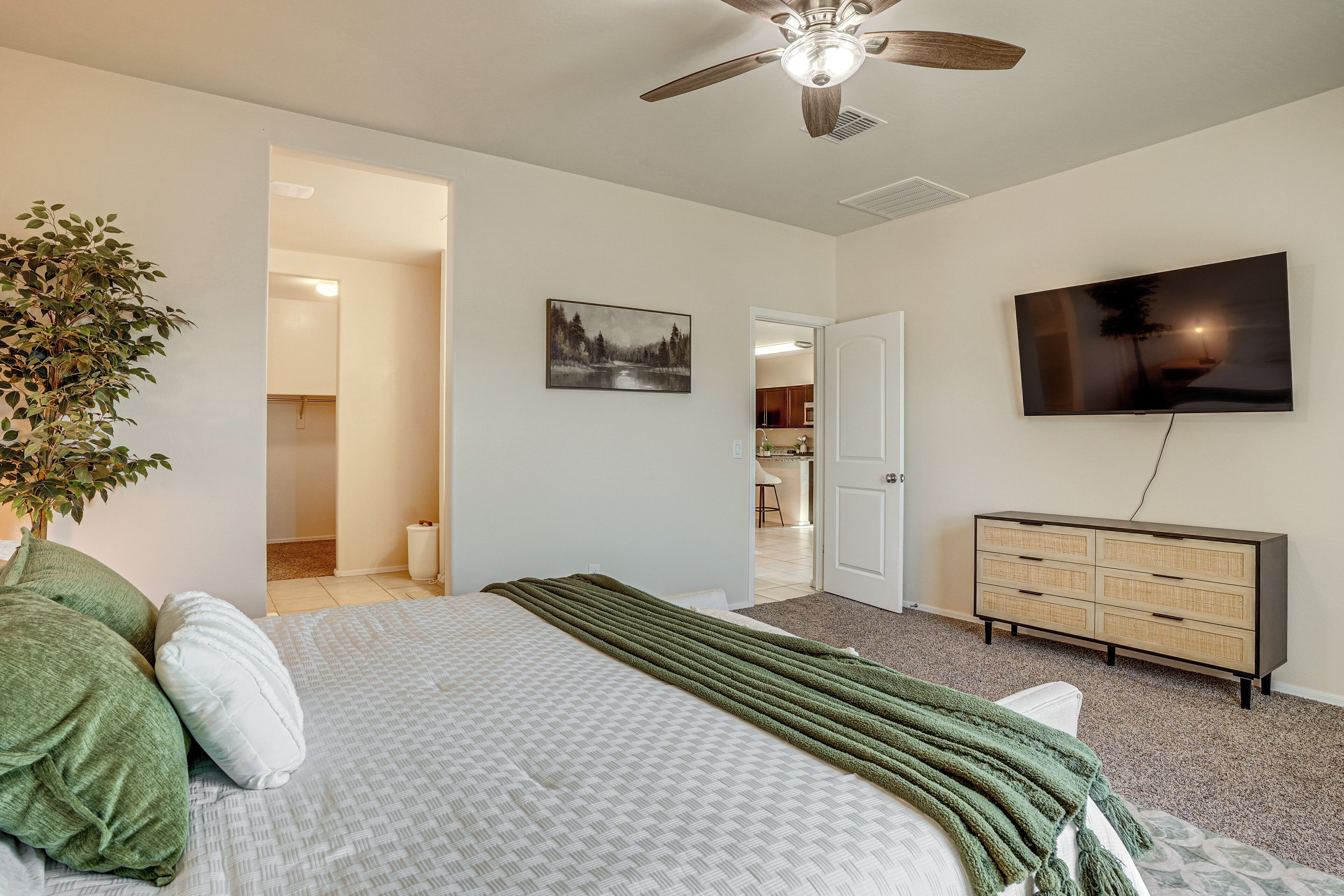 A bedroom with a bed, a dresser, a television, and a ceiling fan.