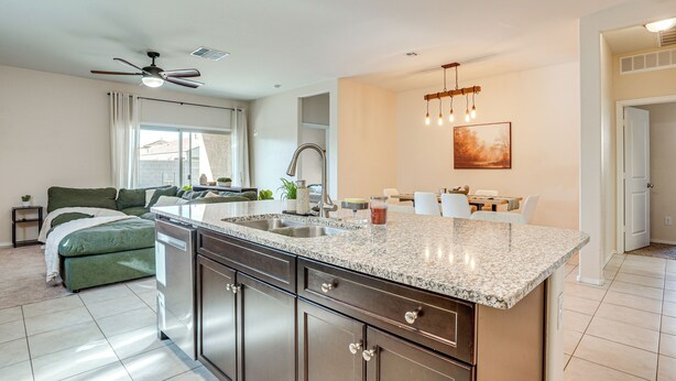 A modern kitchen with a granite countertop, stainless steel cabinets, and a dining area with a table and chairs. - Fenced Yard + Outdoor Games: Buckeye Home! (Buckeye)