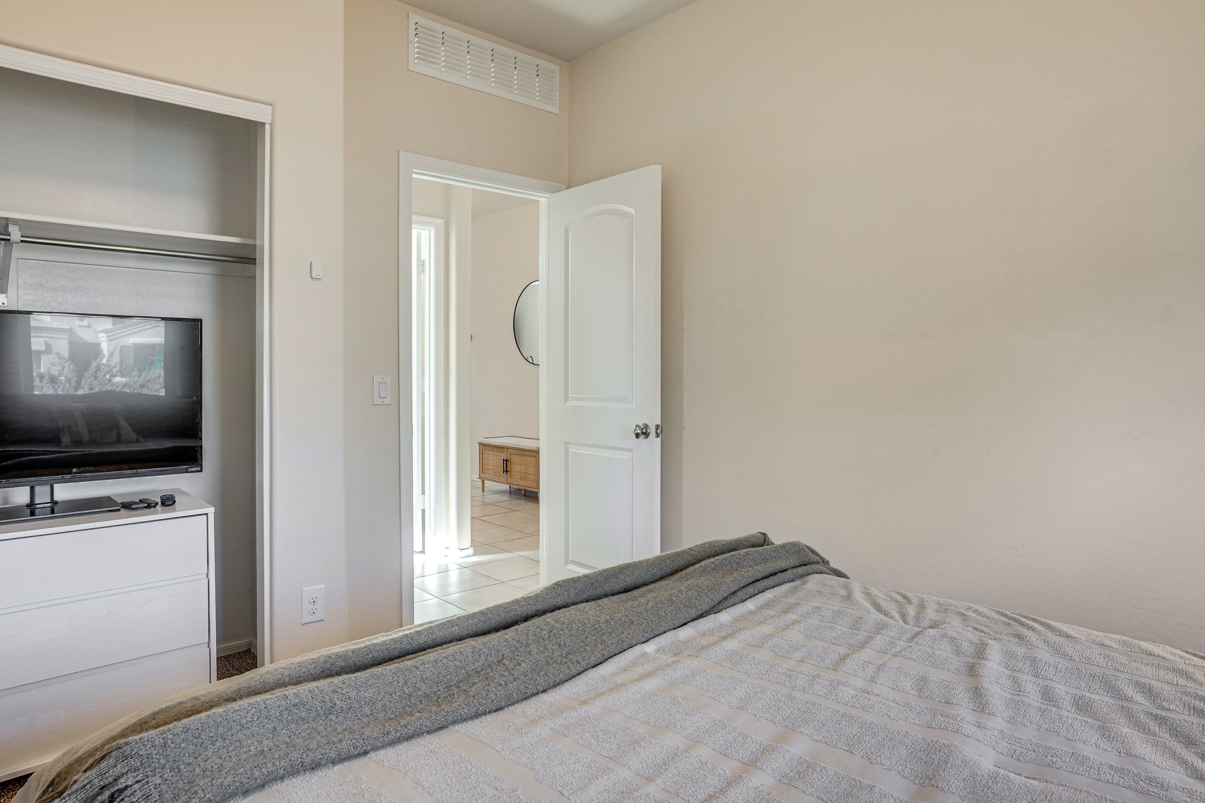A bedroom with a bed, a TV on a dresser, a door leading to a bathroom, and a hallway.