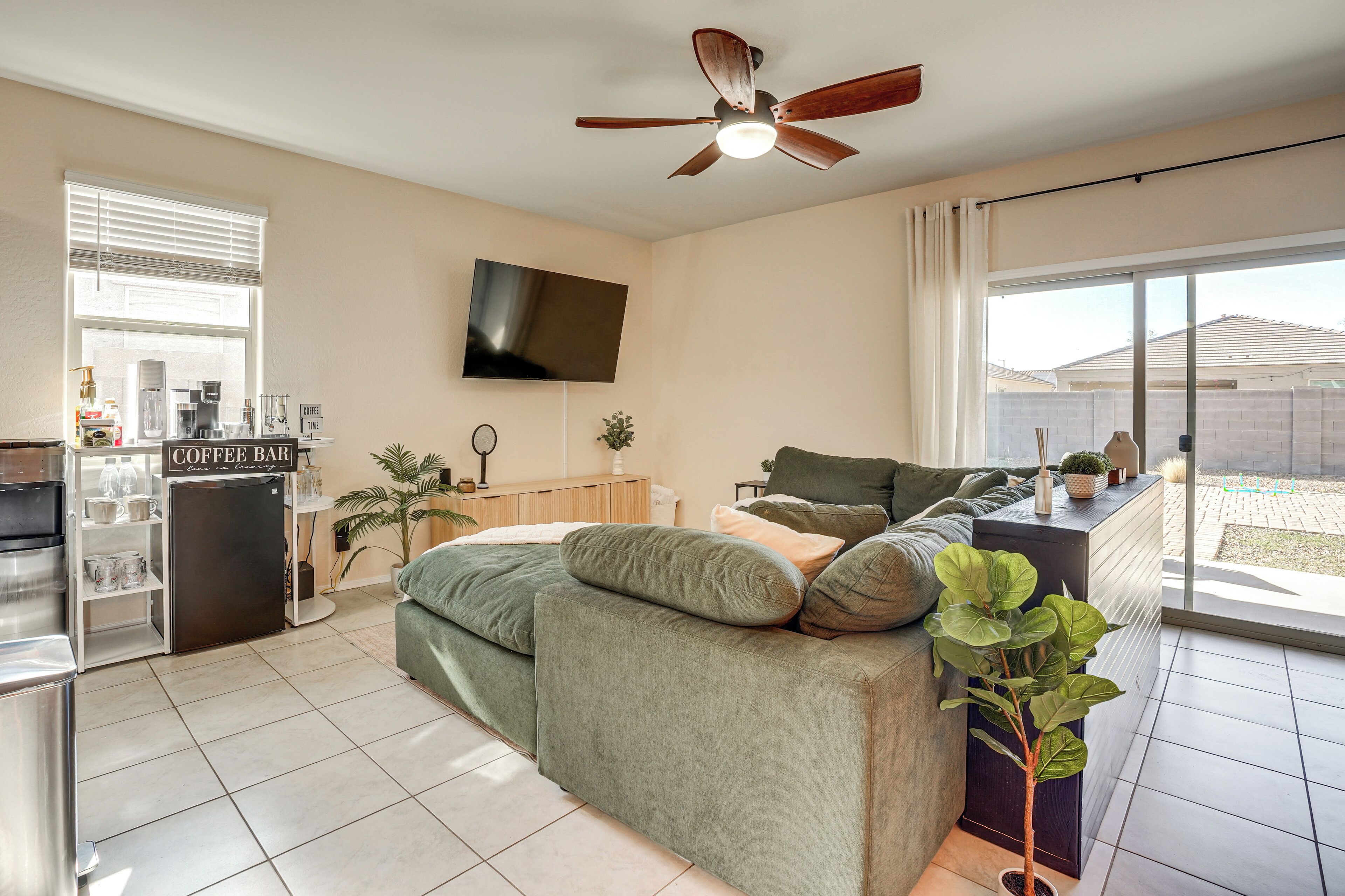 A modern living room with a sofa, a coffee bar, a flat-screen TV, and a ceiling fan.