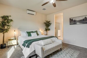A bedroom with a bed, bedside tables, a ceiling fan, and two potted plants. - Fenced Yard + Outdoor Games: Buckeye Home! (Buckeye)