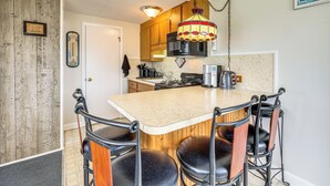 A kitchen with a wooden island, bar stools, a hanging light fixture, and a microwave. - Beach & Pool 318 sqf Cozy Condo East End P-town (Provincetown)