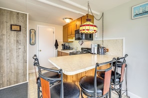A kitchen with a wooden island, bar stools, a hanging light fixture, and a microwave. - Walk to Beach & Pool! East End P-town Condo (Provincetown)