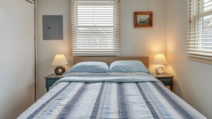 A bedroom with a bed, two bedside lamps, a window with blinds, a picture on the wall, and a power outlet. - Beach & Pool 318 sqf Cozy Condo East End P-town (Provincetown)