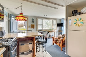 A kitchen with a stove, a dining table with chairs, a hanging light fixture, and a refrigerator. - Walk to Beach & Pool! East End P-town Condo (Provincetown)