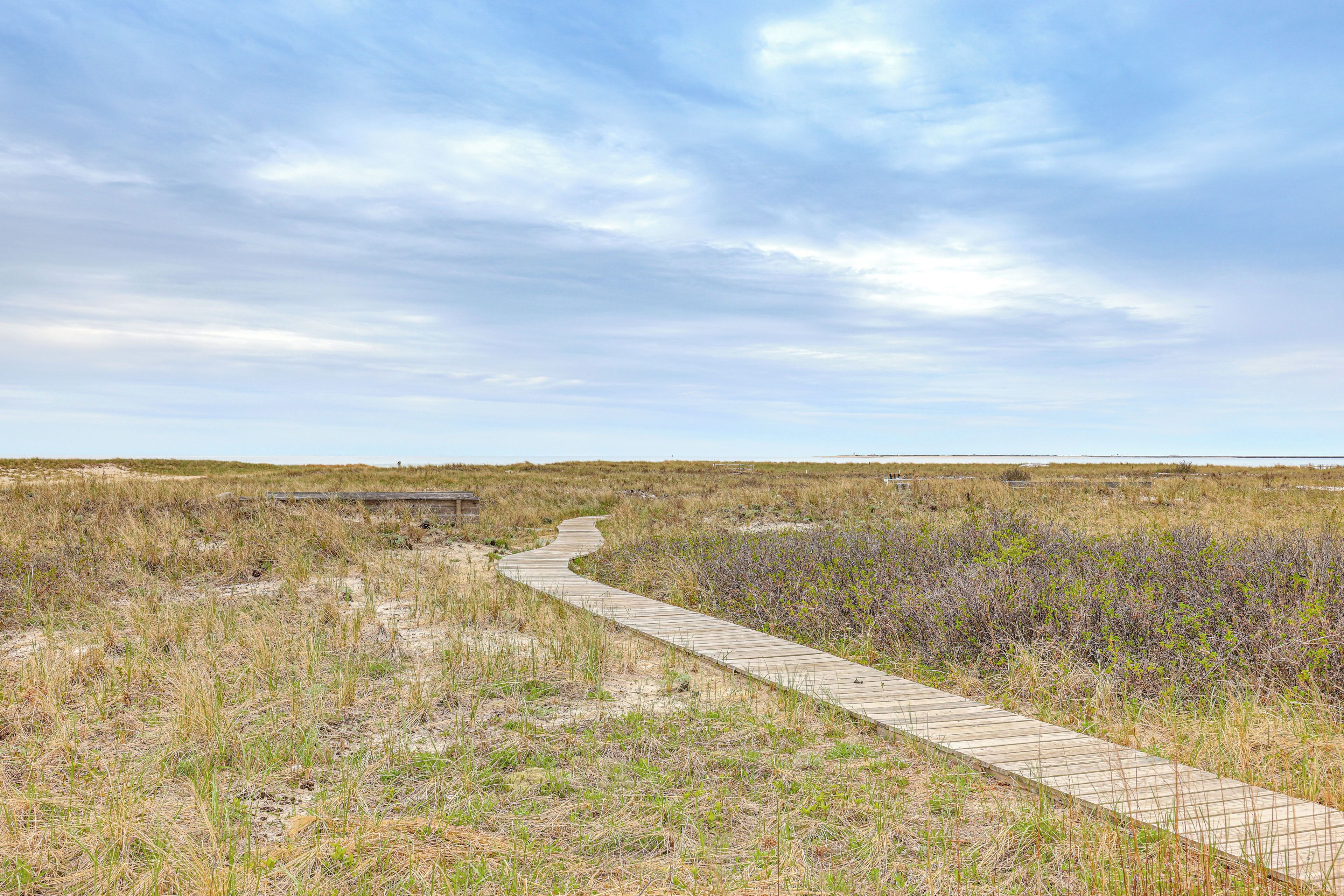 Pasarela de madera que atraviesa un paisaje natural con vegetación escasa y cielo despejado.
