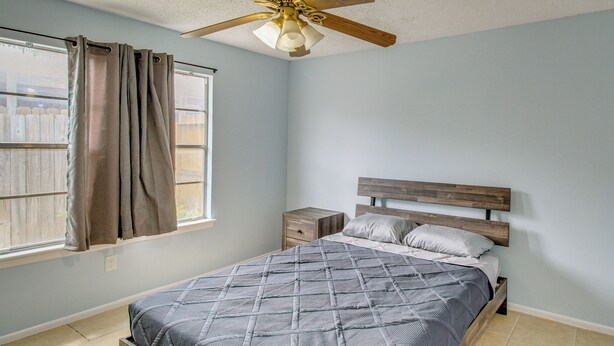 A bedroom with a bed, nightstand, window with curtains, and a ceiling fan. - 2 Private Patios! Family Home in Corpus Christi (Corpus Christi)