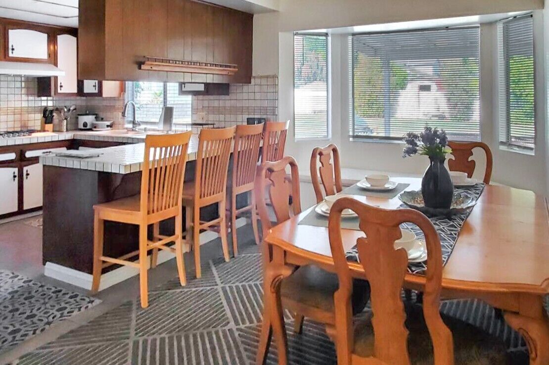 Une cuisine moderne avec des meubles en bois, une table à manger avec des chaises et une fenêtre avec des stores.