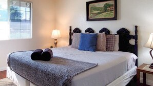 Ein Bett mit einem gemusterten Überwurf, ein Kopfschild mit dekorativen Kissen, eine Nachttischlampe und ein gerahmtes Landschaftsbild an der Wand.
