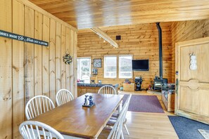 A wooden cabin interior with a dining table, chairs, a sofa, a fireplace, and a television.
