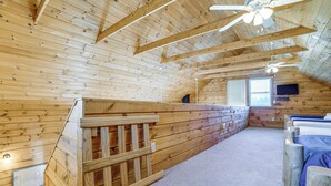 A wooden interior with a sloped ceiling, a built-in bench, a bed with a blue bedspread, and a television mounted on the wall. - Family Friendly! Secluded Worcester Haven w/ Deck (Worcester)