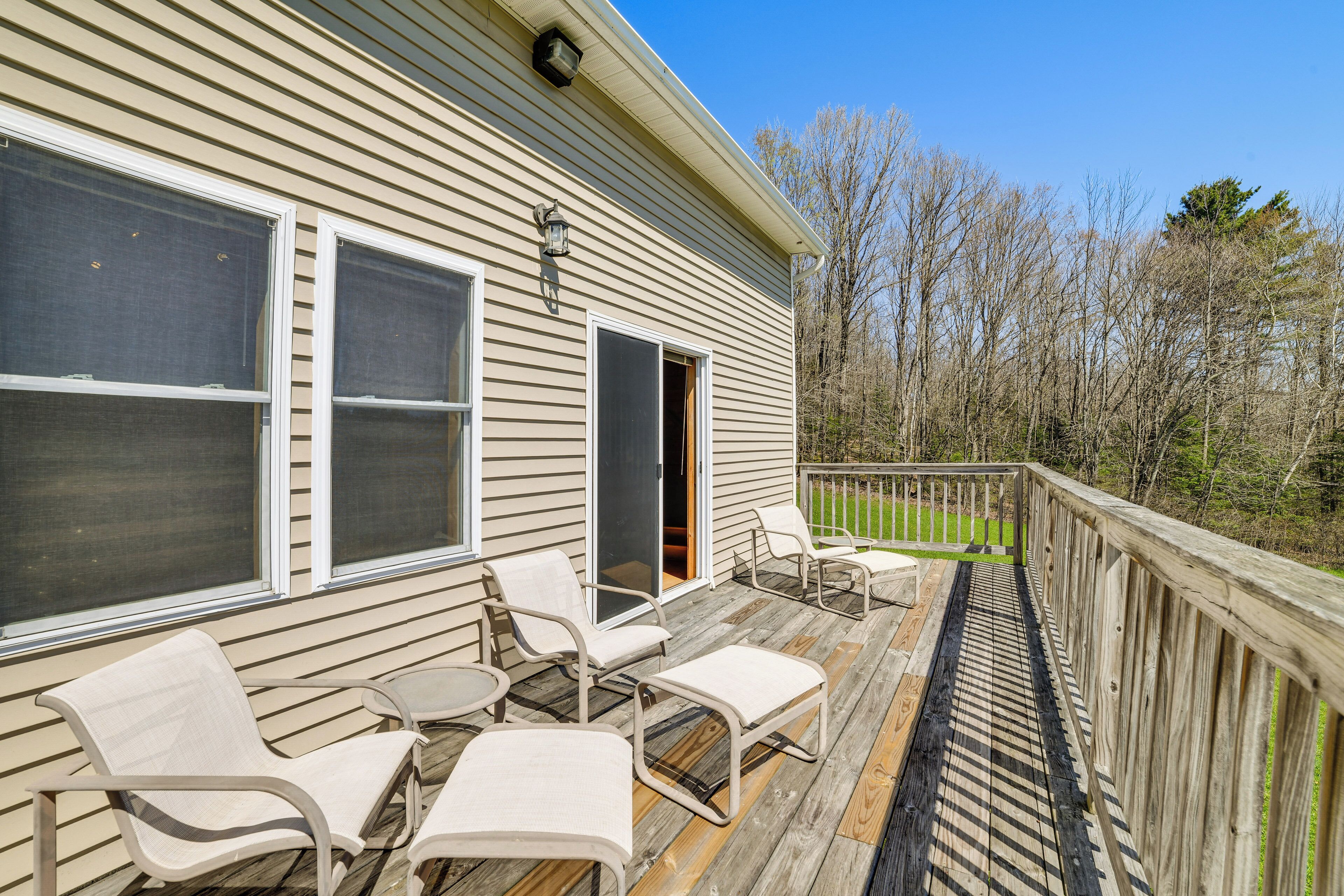 A wooden deck with outdoor furniture, a sliding glass door, and a view of trees.