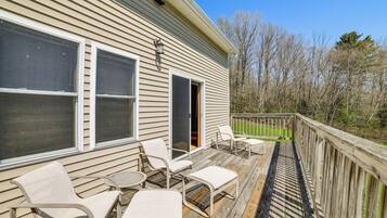 A wooden deck with outdoor furniture, a sliding glass door, and a view of trees.