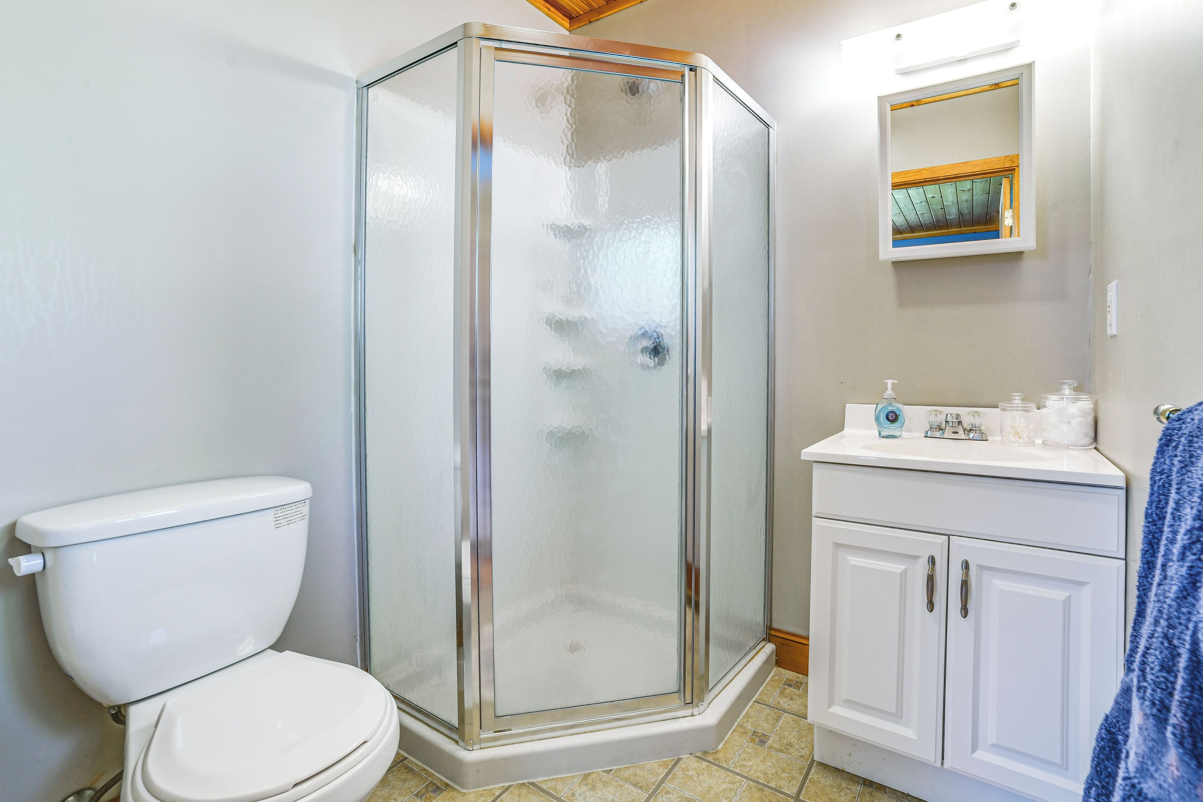 Une salle de bain avec une douche à parois de verre, des toilettes, un lavabo avec des articles de toilette et un miroir.