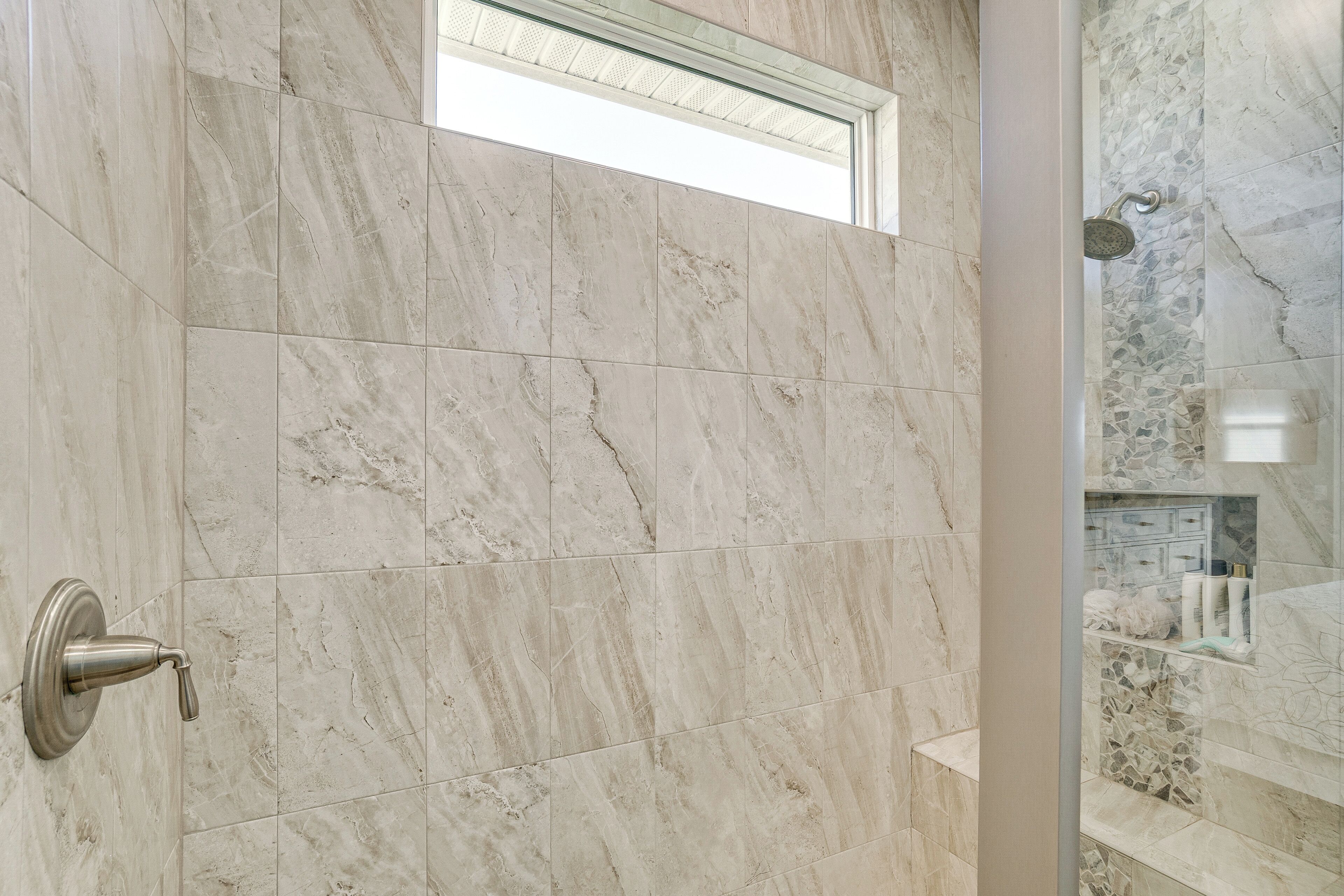 A bathroom with marble tiles, a shower, and a small window.