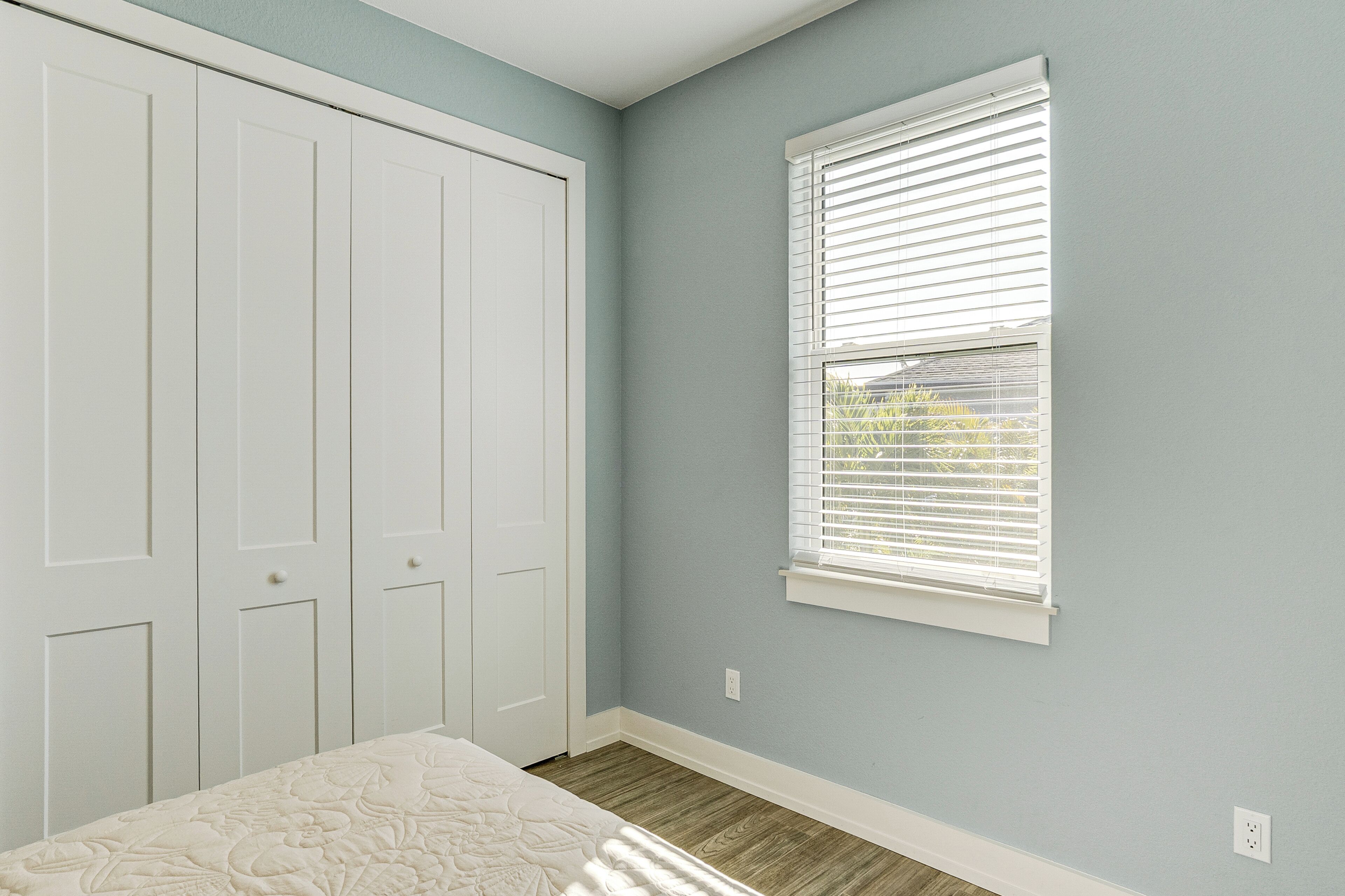 Un dormitorio con un armario grande, una ventana con persianas y suelo de madera.