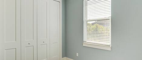 Un dormitorio con un armario grande, una ventana con persianas y suelo de madera.