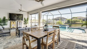 Un patio espacioso con una mesa y sillas de madera, un ventilador de techo y vistas a una piscina.