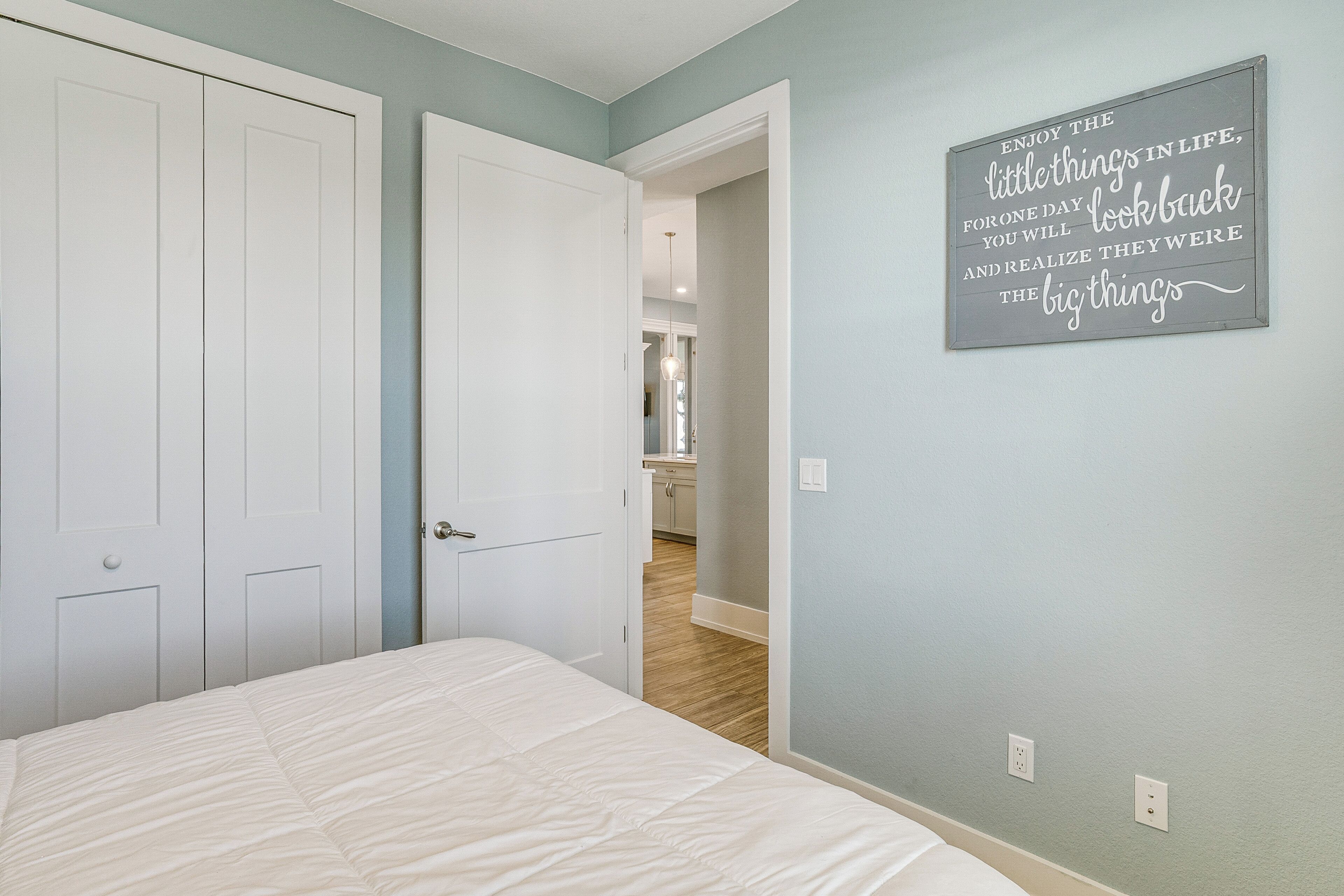 A bedroom with a bed, a door, and a wall with a motivational quote.