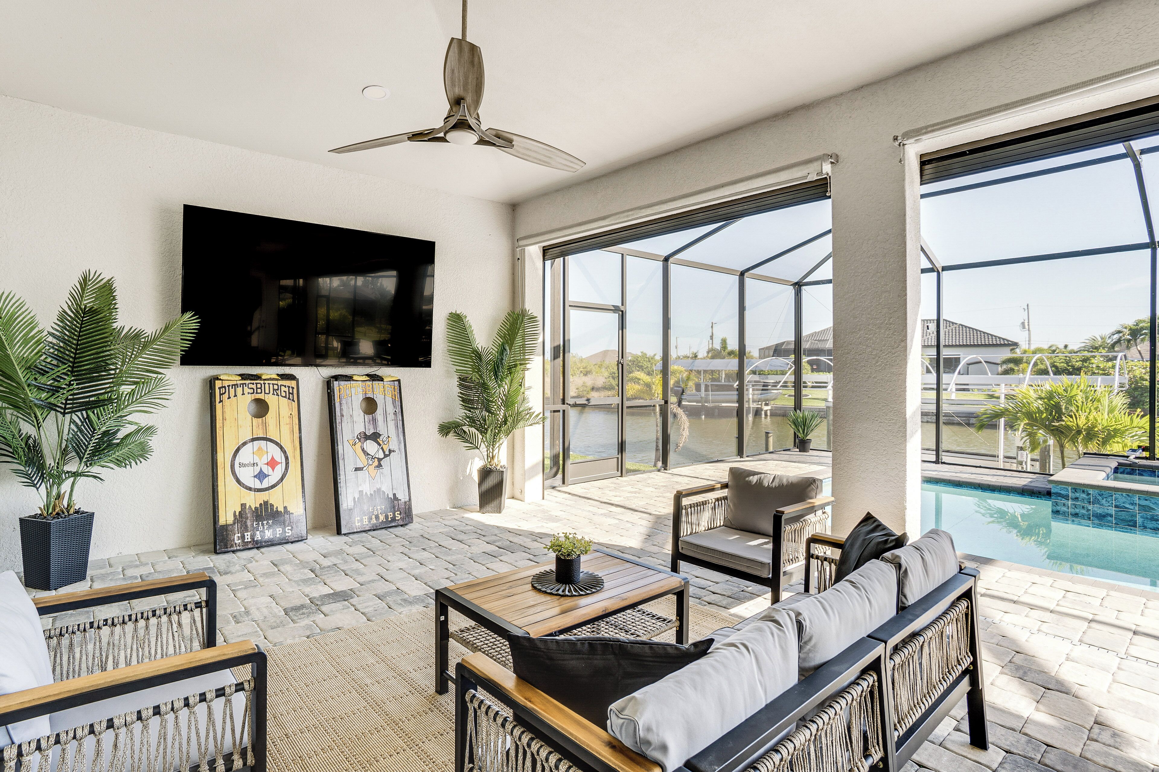 An outdoor patio with seating, a TV, and a pool view.