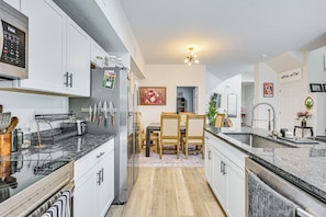 A modern kitchen with white cabinets, a granite countertop, and a dining area with wooden chairs. - Tampa North Aero Park Townhome: Near Downtown! (Lutz)